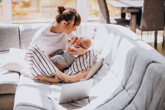 Jeune maman avec son enfant travaillant à la maison sur un ordinateur