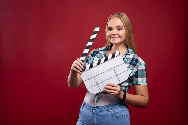 Jeune mannequin blonde tenant un film vierge filmant un panneau de battant et s'amusant.