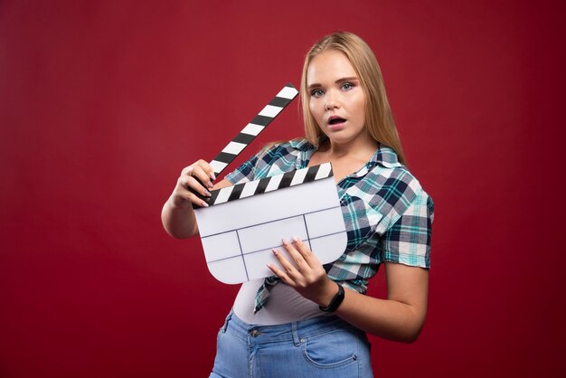 Jeune mannequin blonde tenant un film vierge filmant un panneau de battant et s'amusant.