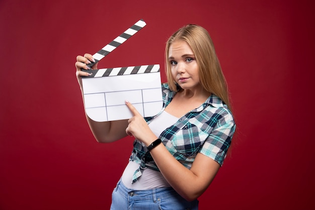 Jeune mannequin blonde tenant un film vierge filmant un panneau de battant et s'amusant.