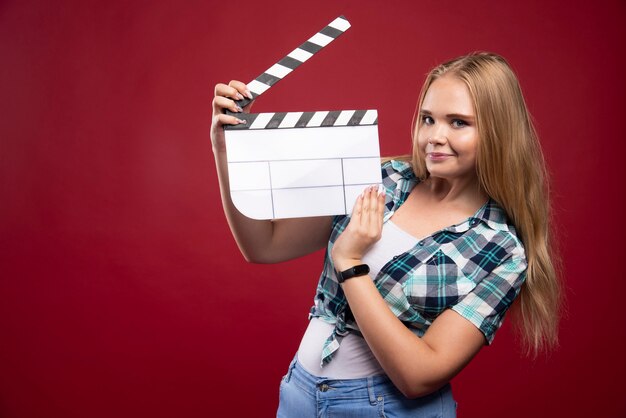 Jeune mannequin blonde tenant une planche de battant de tournage de film vierge.