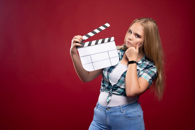 Jeune mannequin blonde tenant une planche de battant de tournage de film vierge.