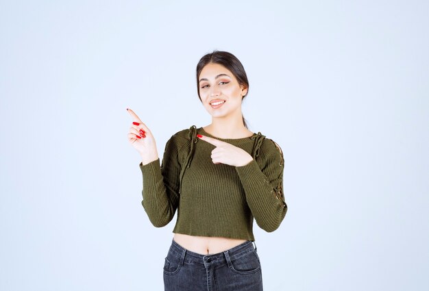 Un jeune mannequin en chemisier vert pointant sur un mur blanc