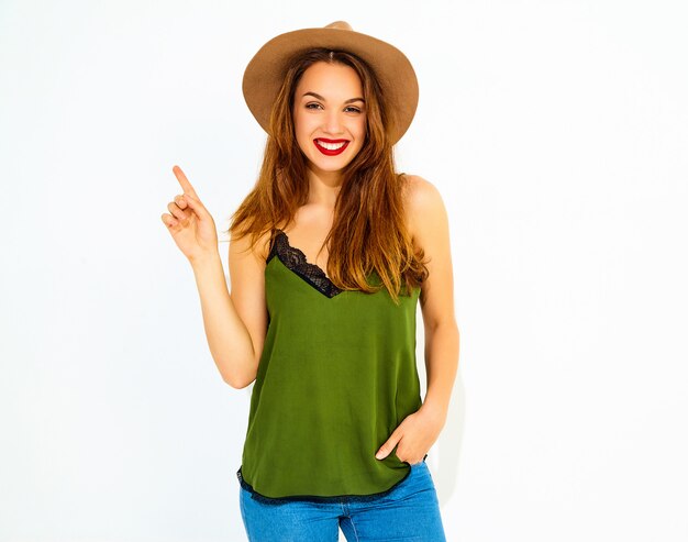 Jeune mannequin élégante dans des vêtements d'été verts décontractés et un chapeau brun avec des lèvres rouges a eu l'idée et elle a levé le doigt. Isolé