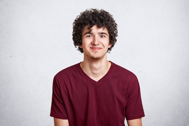 Photo gratuite jeune mec aux cheveux bouclés, robes casual t-shirt marron sur mur de béton blanc. les gens, les jeunes, les vêtements, le concept de publicité.