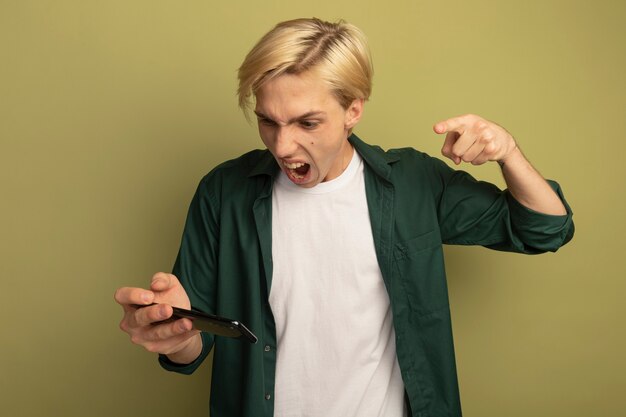 Jeune mec blond en colère portant un t-shirt vert tenant et des points au téléphone