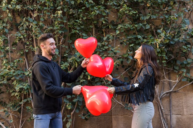 Jeune mec heureux et femme souriante tenant des ballons en forme de coeurs