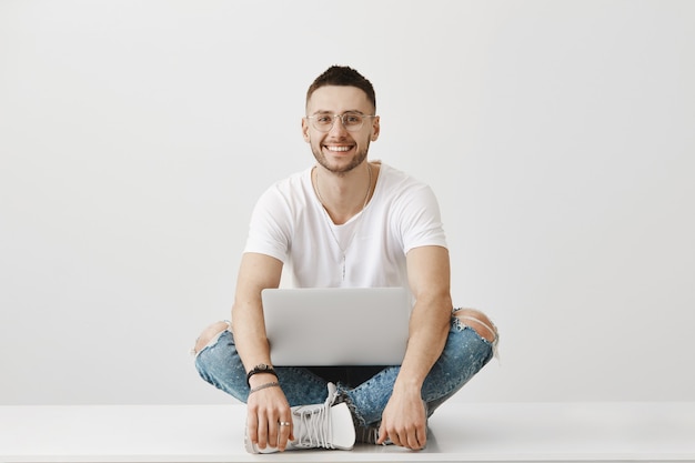 Photo gratuite jeune mec insouciant avec des lunettes posant avec son ordinateur portable