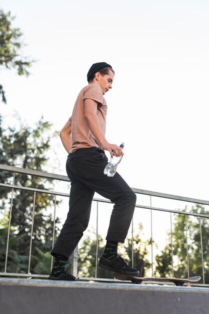 Jeune mec posant avec une planche à roulettes et une bouteille d&#39;eau