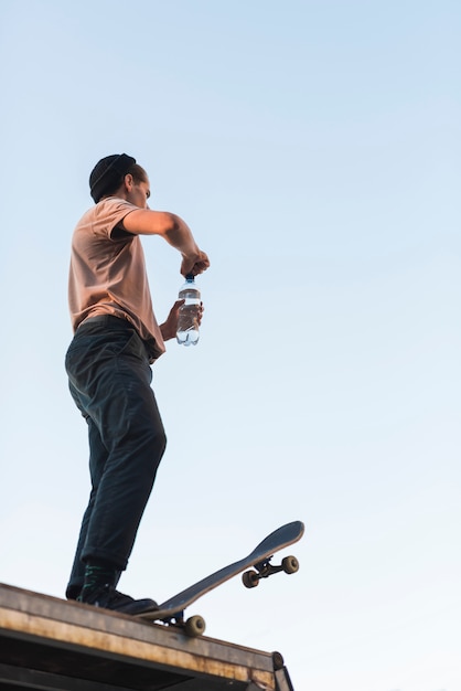 Photo gratuite jeune mec posant avec une planche à roulettes et une bouteille d'eau