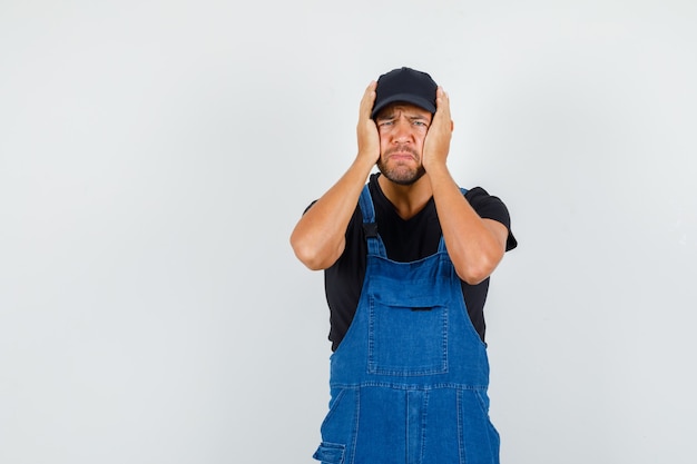 Photo gratuite jeune mécanicien tenant la tête avec les mains en uniforme et à la colère, vue de face.