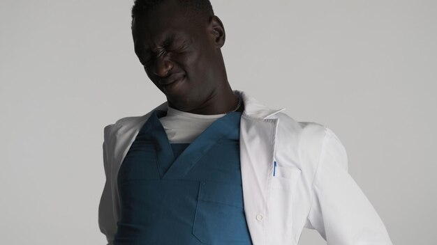Jeune médecin afro-américain fatigué en uniforme faisant des secousses physiques devant la caméra sur fond blanc