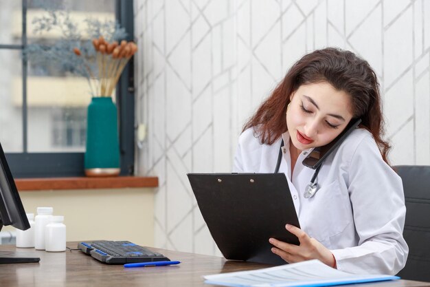 Jeune médecin assis au bureau et parlant au téléphone Photo de haute qualité