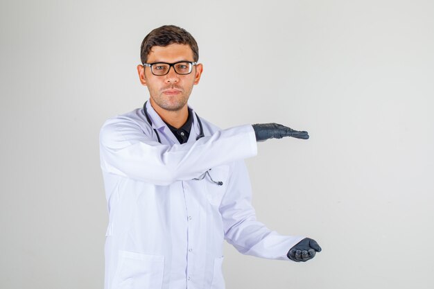 Jeune médecin en blouse blanche avec stéthoscope montrant un signe de grande taille avec les mains