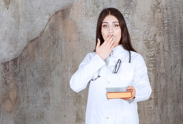 Un jeune médecin bouleversé se tenant la main sur la bouche sur un mur gris