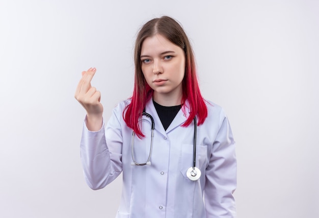 Jeune médecin femme portant une robe médicale stéthoscope montrant le geste de pointe sur un mur blanc isolé