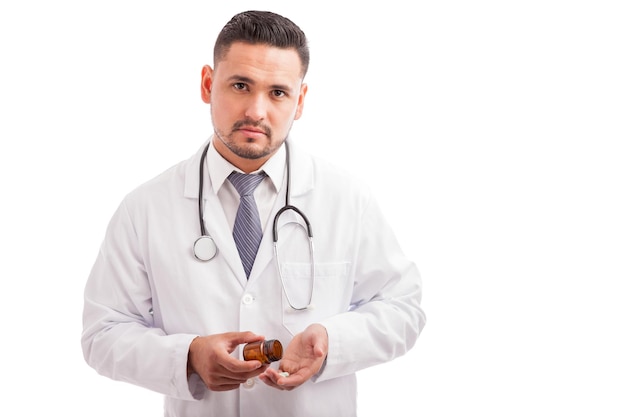 Jeune médecin hispanique confiant prenant des pilules sur ordonnance à partir d'une bouteille sur fond blanc