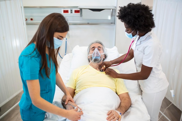 Photo gratuite jeune médecin et infirmière portant un masque chirurgical vérifiant un patient âgé portant un masque à oxygène à pression positive pour aider à respirer dans un lit d'hôpital pendant la pandémie de covid19