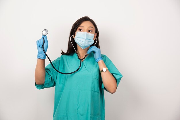 Jeune médecin avec masque à l'aide d'un stéthoscope sur fond blanc. Photo de haute qualité