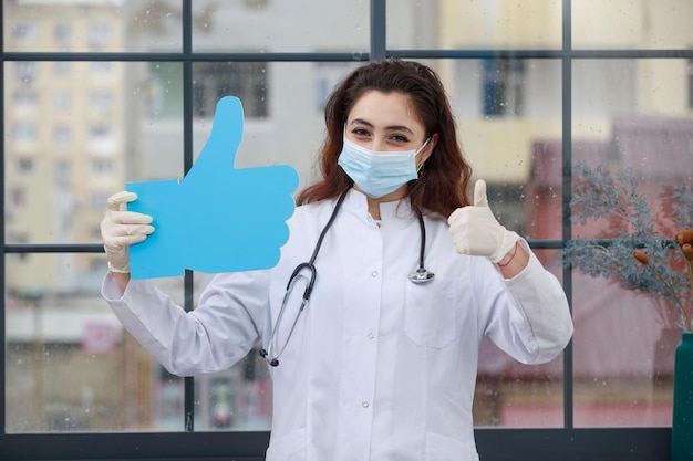 Jeune médecin tenant une bulle d'idée de papier en forme de pouce vers le haut et souriant Photo de haute qualité