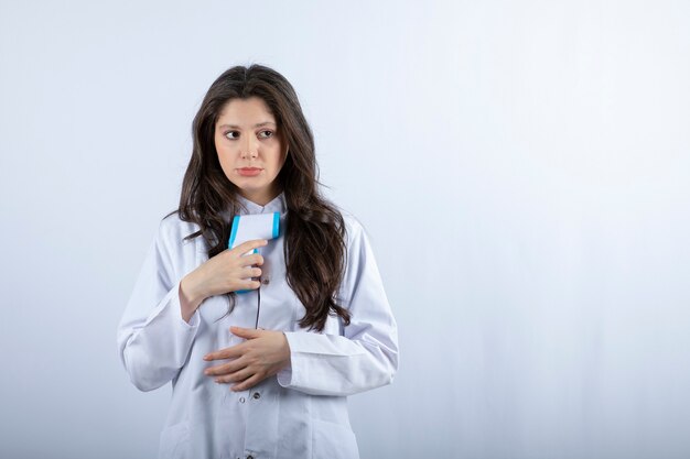 jeune médecin tenant un thermomètre sur un mur blanc.