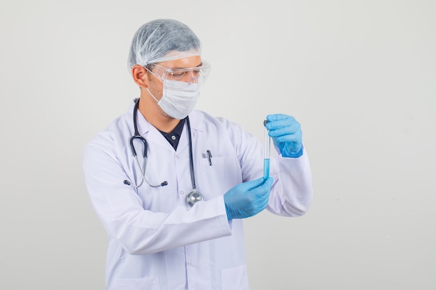 Jeune médecin tenant un tube à essai en blouse blanche, chapeau et gants