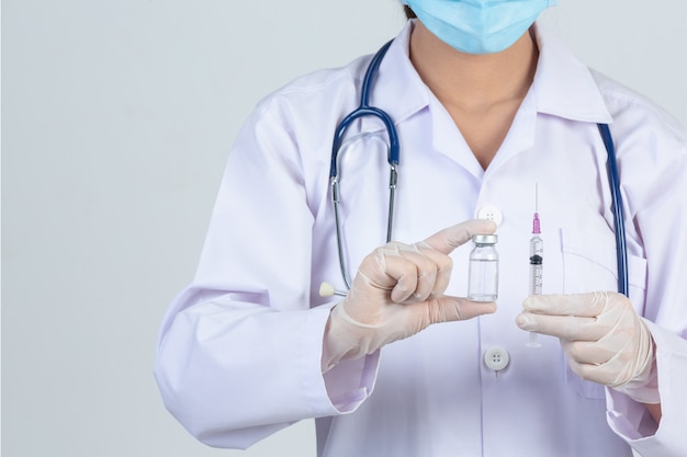 Jeune médecin tient une seringue hypodermique avec des gants en caoutchouc pour flacon de vaccin sur un mur gris.