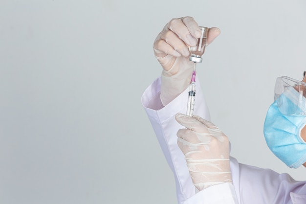 Jeune médecin tient une seringue hypodermique avec des gants en caoutchouc pour flacon de vaccin sur un mur gris.