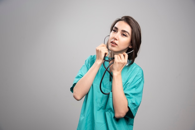 Jeune médecin en uniforme à l'aide d'un stéthoscope sur fond gris. Photo de haute qualité