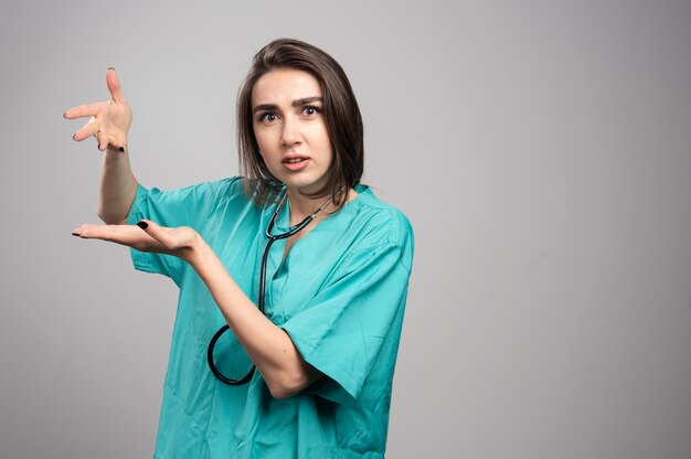 Jeune médecin en uniforme debout sur un mur gris.