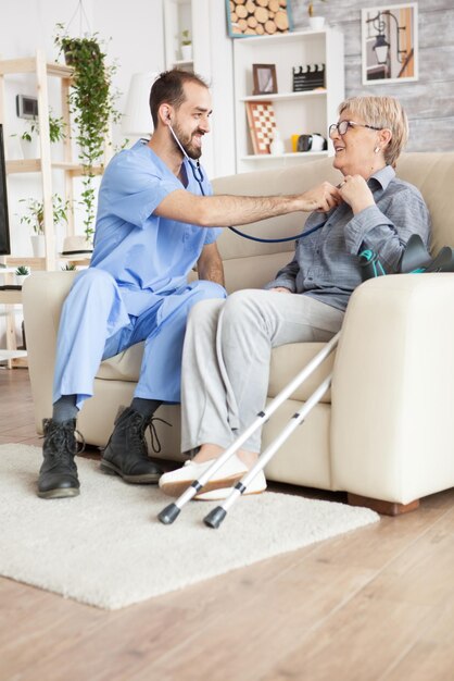 Jeune médecin utilisant un stéthoscope pour écouter les battements de cœur d'une vieille femme dans une maison de retraite.