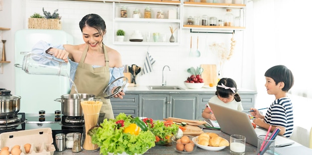 Jeune mère célibataire asiatique faisant de la nourriture tout en prenant soin de son enfant dans la cuisine