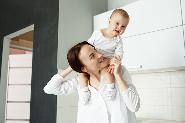 Jeune mère joyeuse portant son bébé sur les épaules et riant