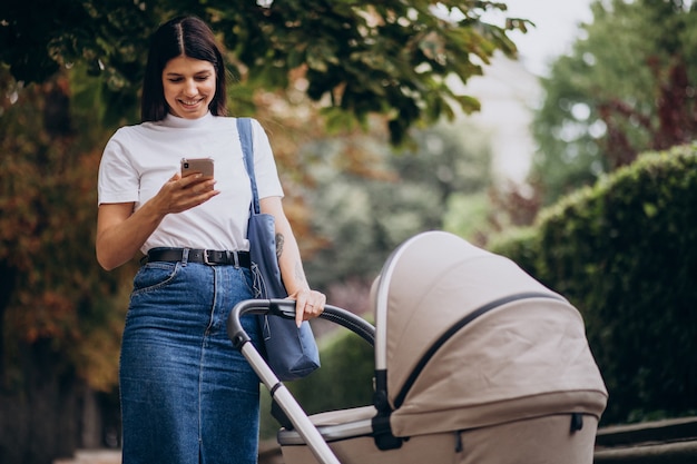 Jeune mère marchant avec poussette dans le parc et parler au téléphone