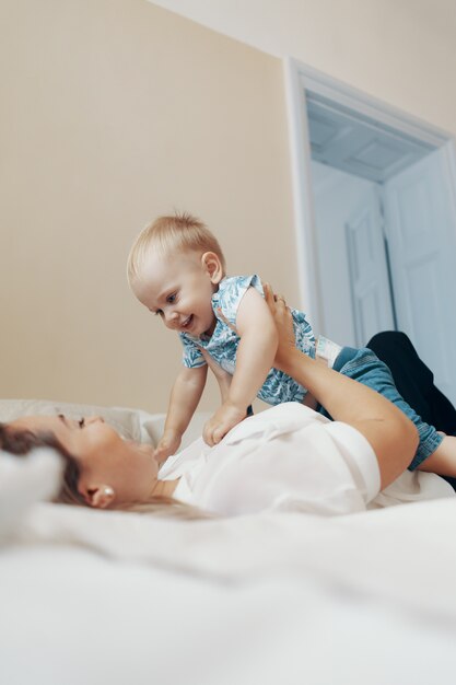 Jeune mère s'amusant à jouer à des jeux actifs drôles avec un enfant mignon dans sa chambre