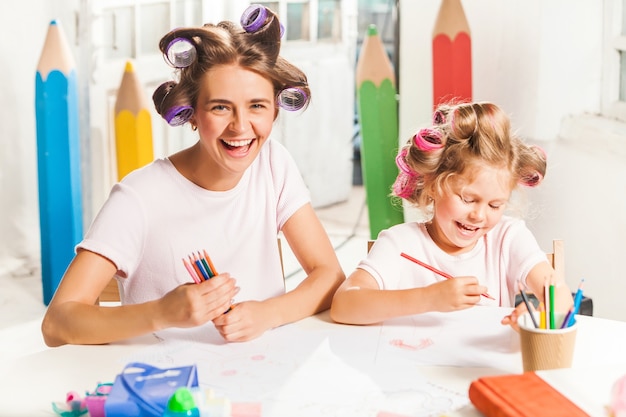 La jeune mère et sa petite fille dessinant avec des crayons à la maison