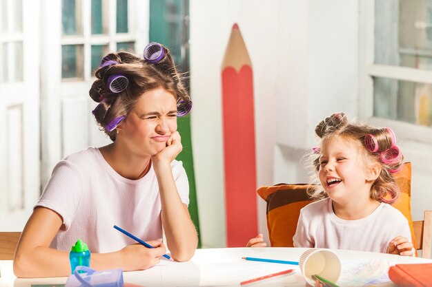 La jeune mère et sa petite fille dessinant avec des crayons à la maison