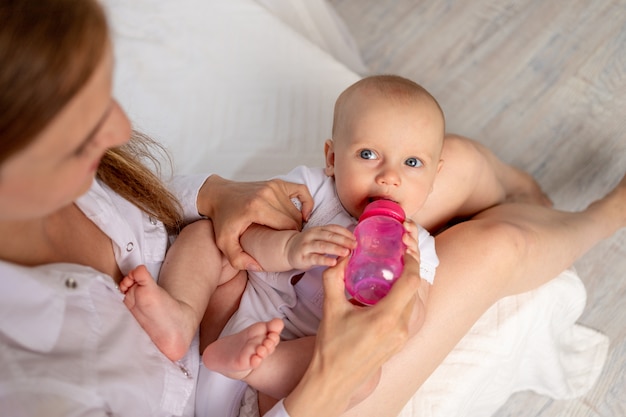 Une Jeune Mere Tient Un Bebe De 6 Mois Dans Ses Bras Et Le Nourrit Avec Du Lait D Une Bouteille Sur Un Lit Blanc L Amour De La Mere Et De L Enfant La Une Jeune Mere Tient Un Bebe De 6 Mois Dans Ses Bras Et Le Nourrit Avec Du Lait D Une Bouteille Sur Un Lit Blanc L Amour De La Mere Et De L Enfant La