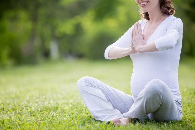 Jeune modèle enceinte méditant sur la pelouse. Fermer