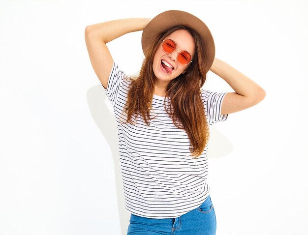 Jeune modèle de femme qui rit élégant dans des vêtements d'été décontractés en chapeau brun avec du maquillage naturel isolé sur mur blanc.