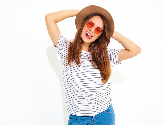 Jeune modèle de femme qui rit élégant dans des vêtements d'été décontractés en chapeau brun avec du maquillage naturel isolé sur mur blanc.