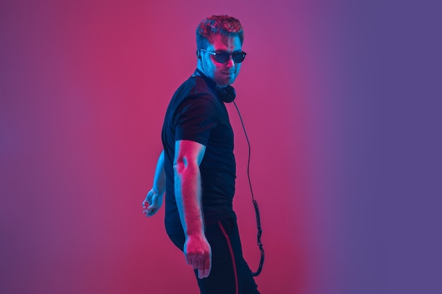 Jeune musicien caucasien au casque chantant sur un mur dégradé rose-violet à la lumière du néon. Concept de musique, passe-temps, festival. Hôte de fête joyeux, DJ, debout. Portrait coloré de l'artiste.