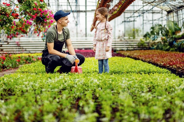 Jeune ouvrier de serre parlant à une petite fille tout en nourrissant des plantes