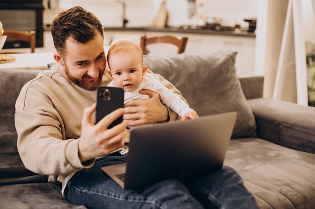 Jeune père assis avec sa petite fille et utilisant un ordinateur à la maison