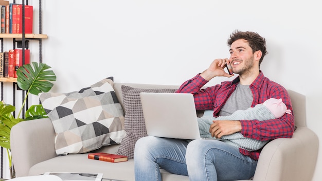 Jeune père avec bébé parler au téléphone et à l'aide d'un ordinateur portable