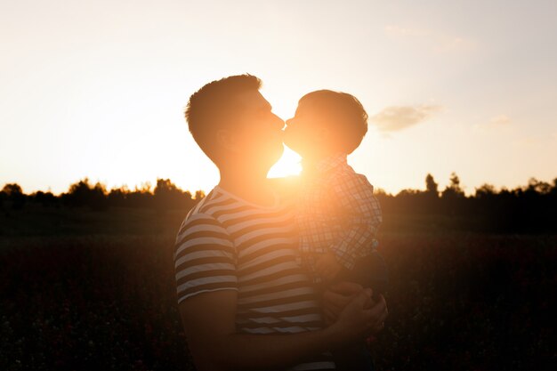 Jeune père embrasse son fils enfant en bas âge sur le champ de fleurs de printemps au coucher du soleil.