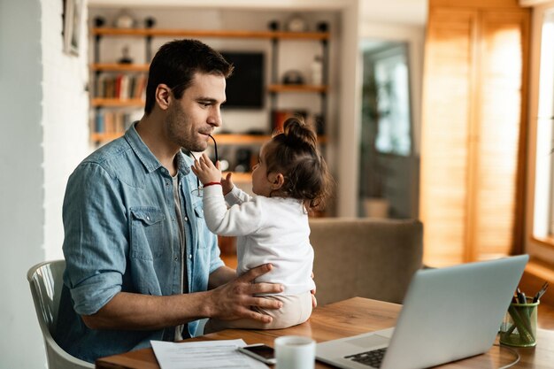 Jeune père s'amusant avec sa petite fille tout en travaillant à la maison