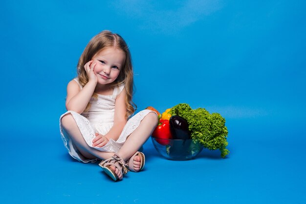 Jeune petite fille avec des légumes sur un mur bleu