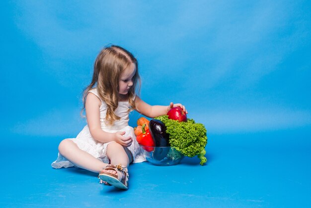 Jeune petite fille avec des légumes sur un mur bleu