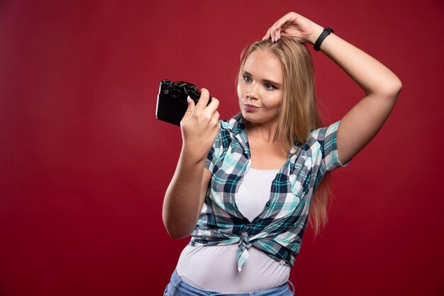 Jeune photo blonde tenant un appareil photo professionnel et prend son selfie dans des positions charmantes et confiantes.